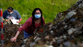 Female Fresno State student wearing a mask and glasses climbing a hillside